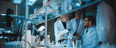 Group of smiling researchers gathered around microscope bench